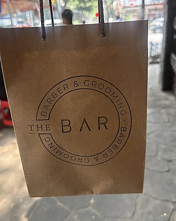 Bolsa de papel kraft con el sello circular de The Bar, Barber & Grooming
