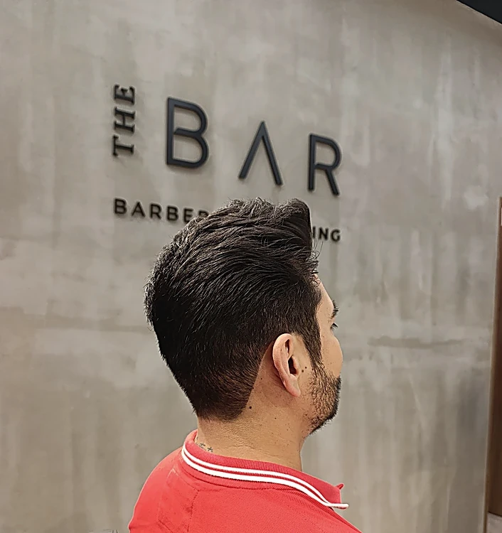 Corte corto texturizado con laterales bajos, visto de espaldas frente al logo de The Bar en el muro de concreto